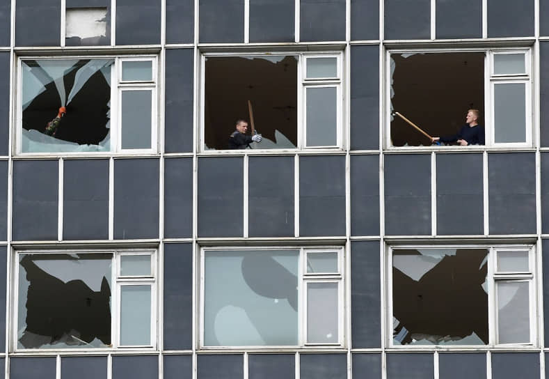 Люди убирают разбитые стекла с окон здания, поврежденного из-за обстрела во Львове
