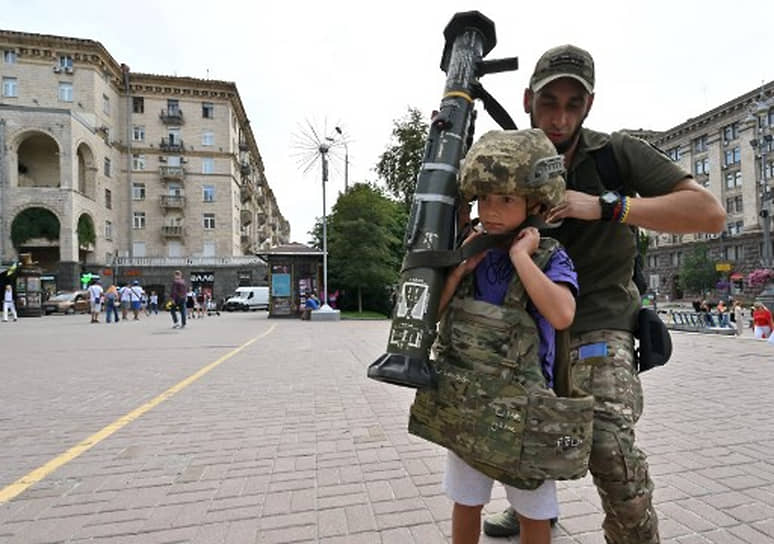 Украинский военнослужащий помогает мальчику надеть бронежилет для фото у волонтерского пункта в центре Киева