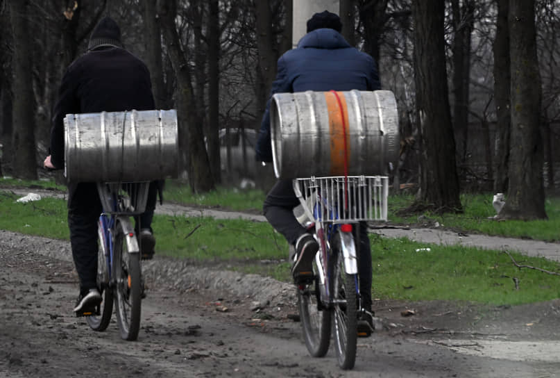 Мужчины на велосипедах перевозят металлические бочки