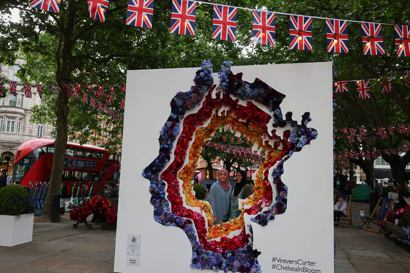 Люди делают селфи перед цветочной экспозицией с изображением королевы