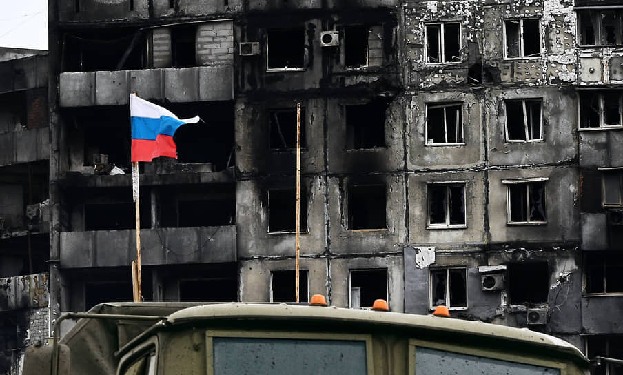 Российский флаг на фоне разрушенного здания в Мариуполе