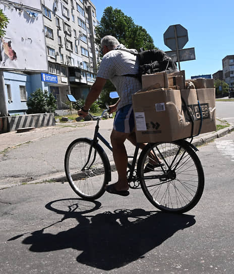 Мужчина на велосипеде с коробками на багажнике едет по улице Бердянска