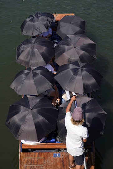 Люди под зонтиками на лодке в Кембридже (Великобритания)