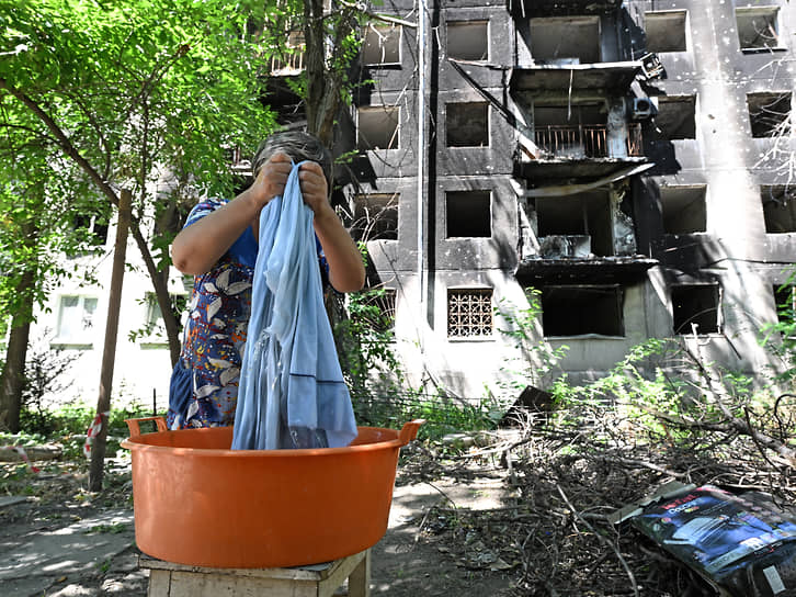 Мариуполь. Женщина стирает белье во дворе разрушенного многоквартирного дома