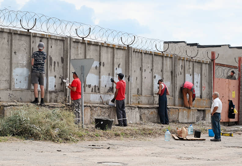 Мариуполь. Рабочие заделывают в заборе пробоины от пуль и осколков
