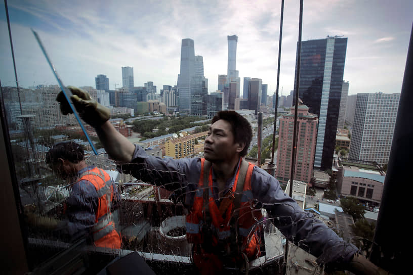 Пекин. Рабочие на подвесной платформе моют окна офисного здания