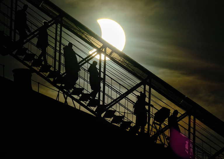 Туристы спускаются с колоннады Исаакиевского собора в Санкт-Петербурге во время солнечного затмения