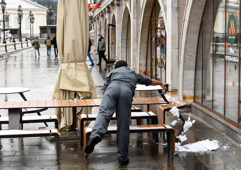 Сотрудник ресторана убирает снег со столов на Манежной площади