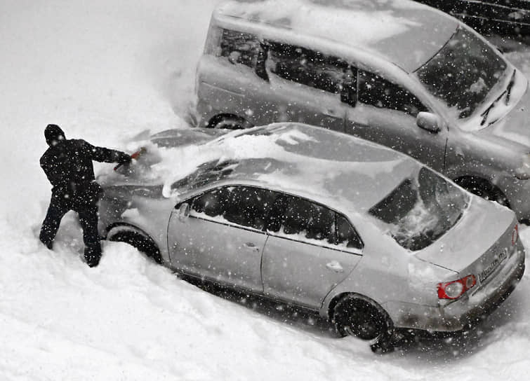 Водитель очищает от снега припаркованный автомобиль