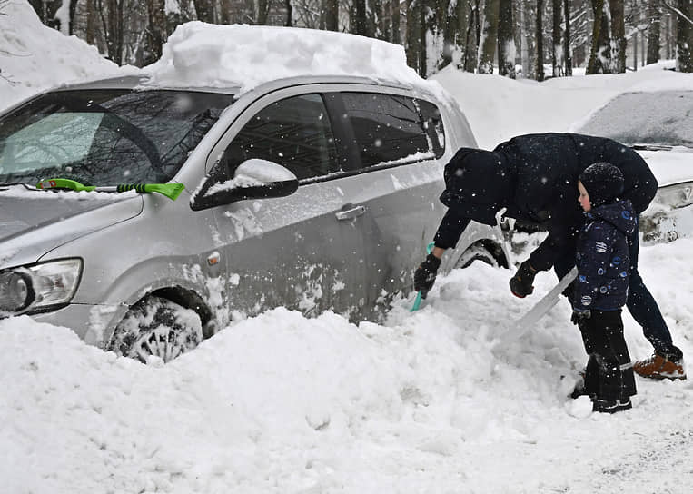 Водитель очищает от снега припаркованный автомобиль