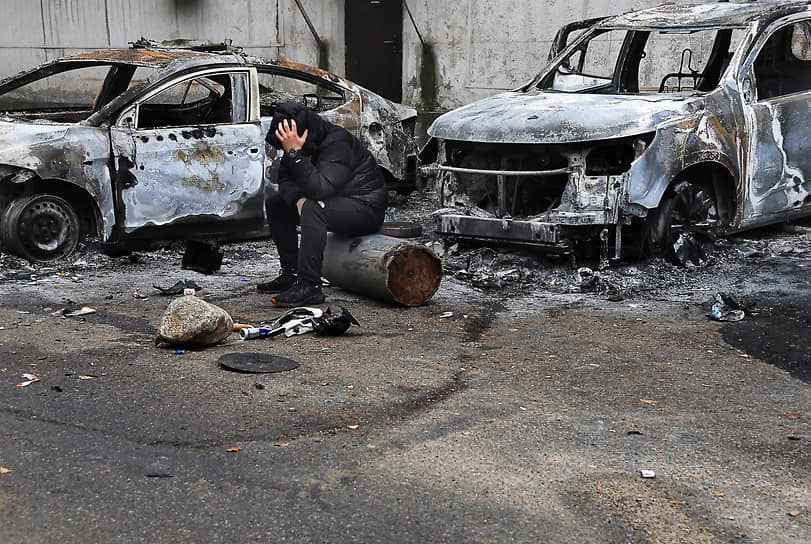Мужчина сидит у сожженных автомобилей после протестов в Алматы