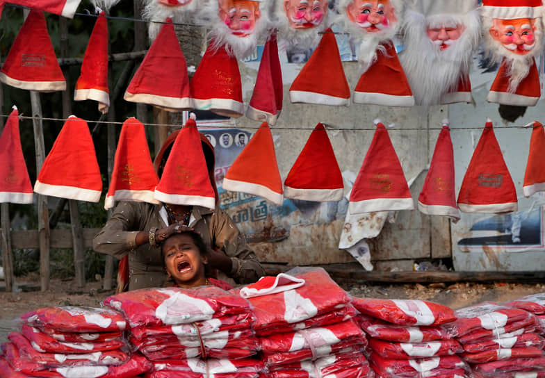 Хайдарабад, Индия. Торговец рождественскими товарами расчесывает ребенка