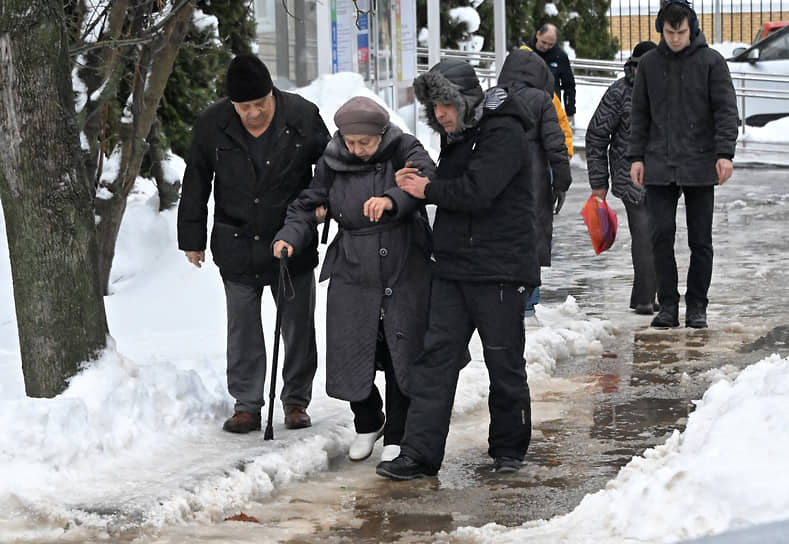 Мужчины помогают пожилой женщине идти по скользкому тротуару