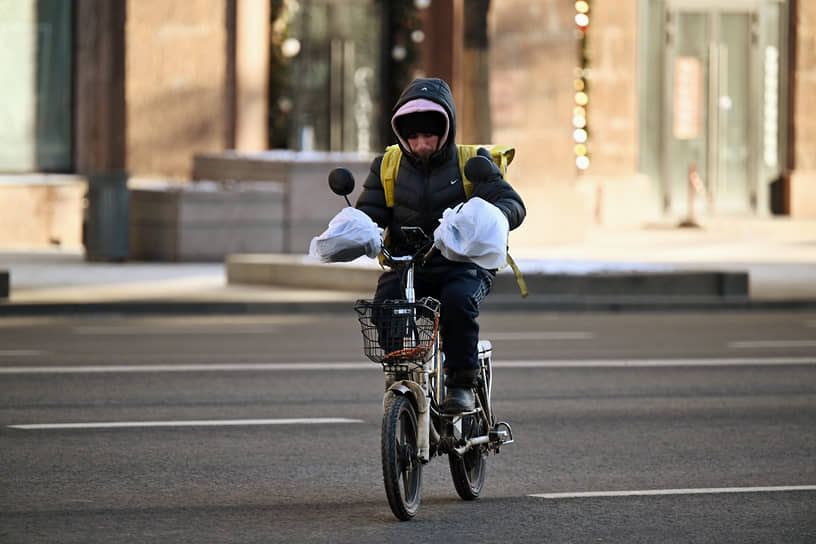 Курьер едет по улице на велосипеде 