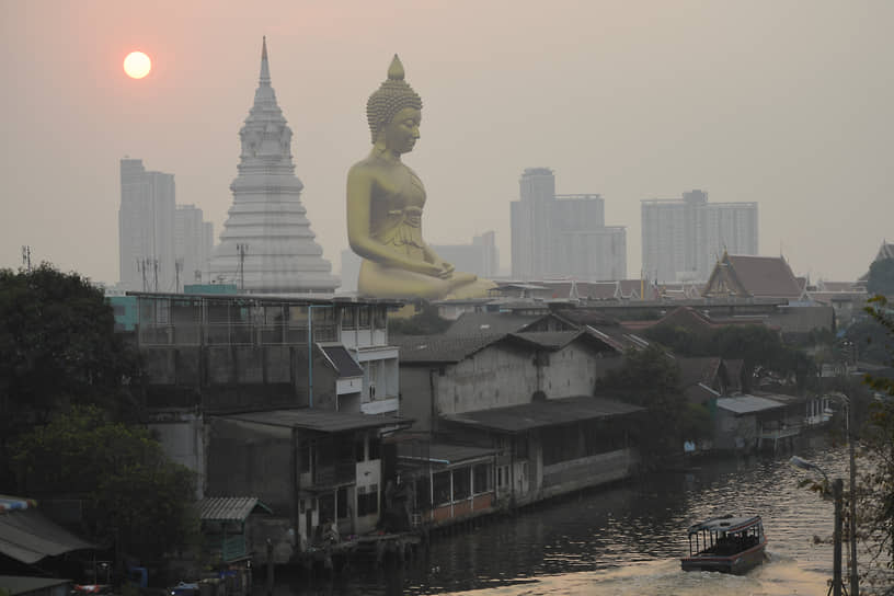 Бангкок, Таиланд. Золотая статуя Будды у храма Ват Пакнам Бхасичароен на фоне городской дымки