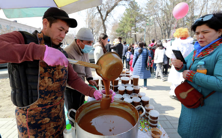 Мужчина наливает посетительнице праздничной ярмарки в Бишкеке сумаляк — главное блюдо Навруза