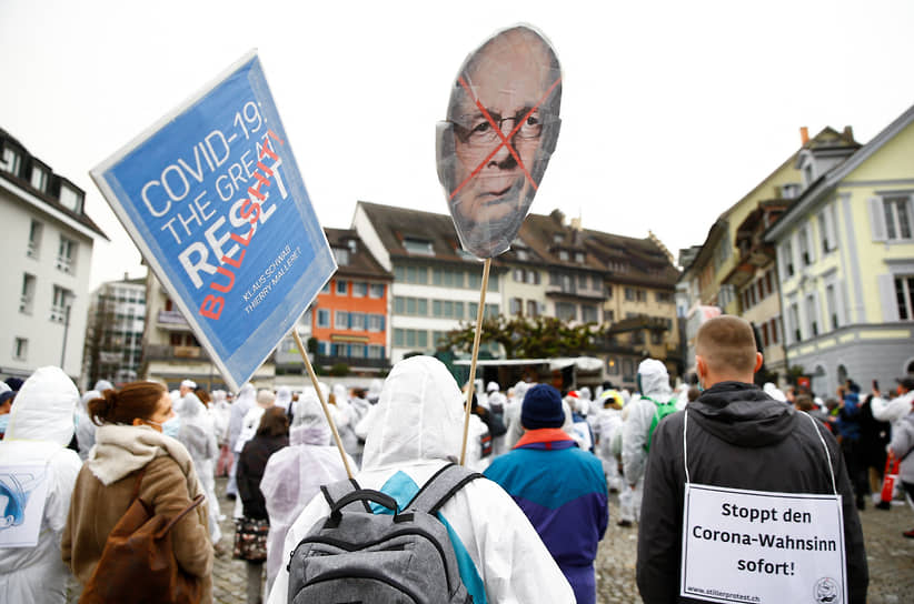 Демонстрант держит плакат с изображением Клауса Шваба во время акции протеста в связи с пандемией коронавируса в Цуге, Швейцария. 2021 год
