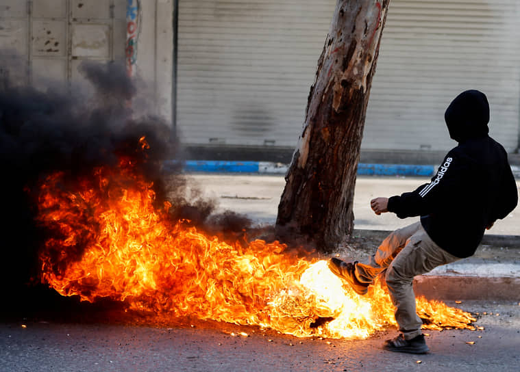 Западный берег реки Иордан. Палестинец пинает горящий предмет во время столкновений с израильскими солдатами
