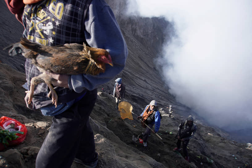 Жители деревни ждут около кратера вулкана Бромо в Индонезии, пока индуисты бросают в него подношения на церемонии Ядня Касада