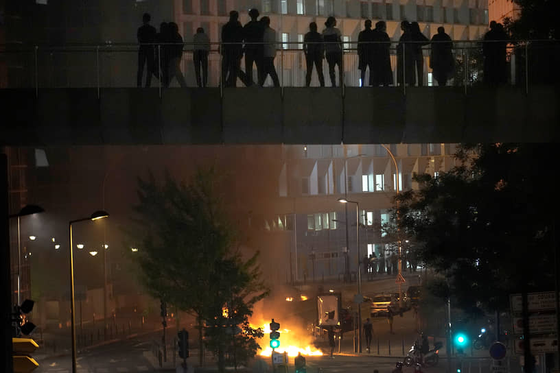 Люди на мосту наблюдают за протестующими, сжигающими мусор в Нантере