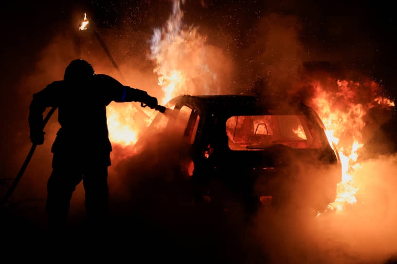 Пожарный тушит подожженный протестующими автомобиль