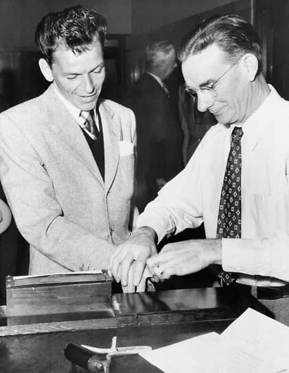 Американский певец и актер Фрэнк Синатра (слева) сдает отпечатки пальцев после подачи заявки на разрешение для ношения оружия в штате Калифорния, 1947 год
