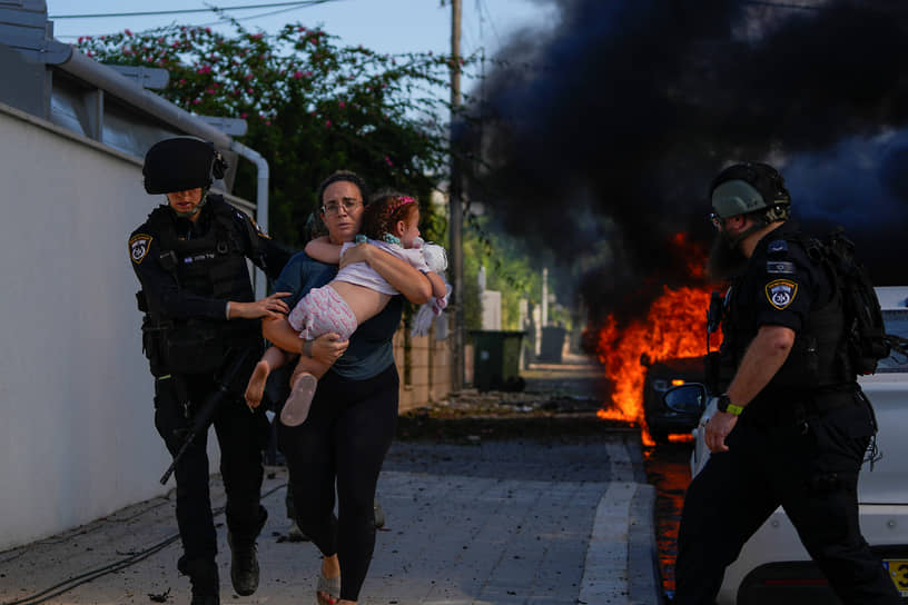 Полицейские эвакуируют женщину с ребенком из зоны падения ракеты в Ашкелоне (Израиль)