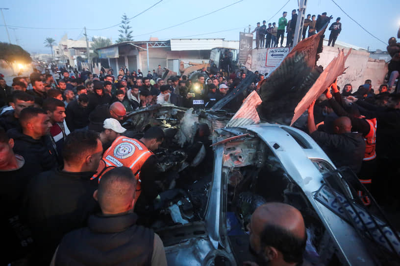 Палестинцы окружают автомобиль, пострадавший от израильского авиаудара в Рафахе (сектор Газа)