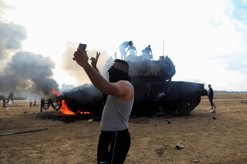 Палестинец делает селфи возле горящего израильского танка на границе сектора Газа и Израиля