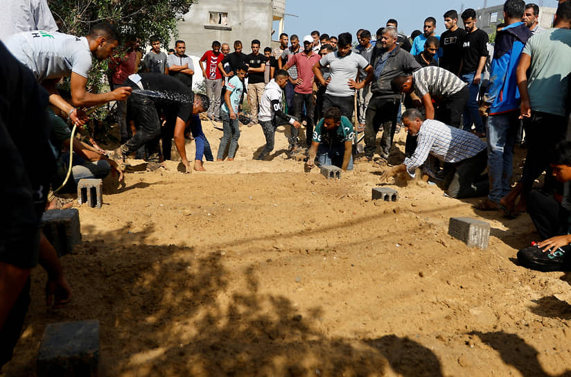 Люди окропляют водой могилы после захоронения тел палестинцев, погибших в результате израильских ударов по городу Хан-Юнис на юге сектора Газа