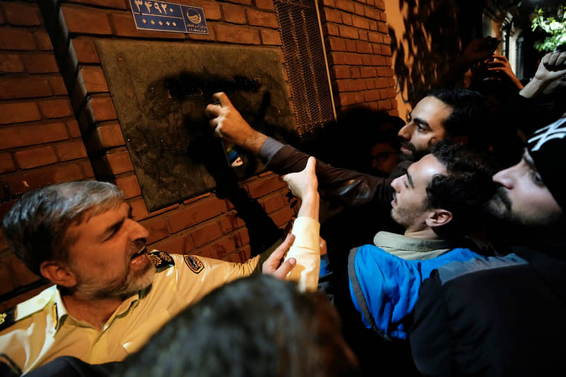 Полицейский останавливает протестующего, который распыляет краску на вывеску посольства Франции в Тегеране