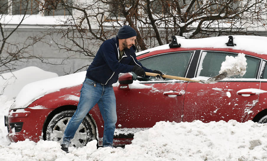 Мужчина чистит машину от снега 