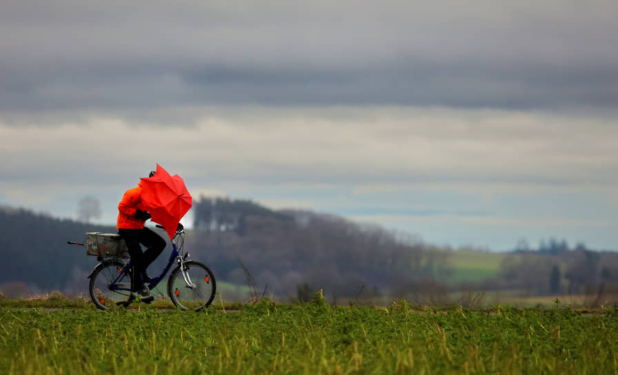 Ридлинген, Германия. Велосипедист прикрывается зонтом от дождя и ветра
