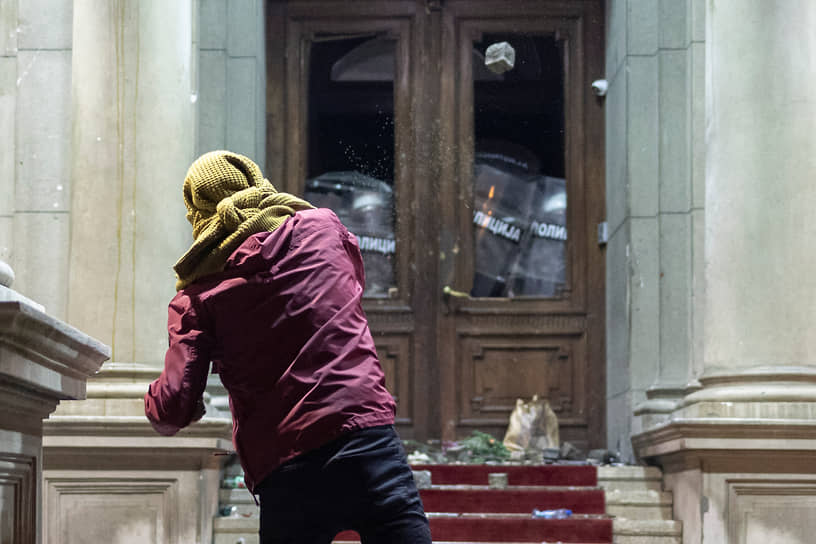 Протестующий бросает камень в полицейских, охраняющих дверь столичной администрации
