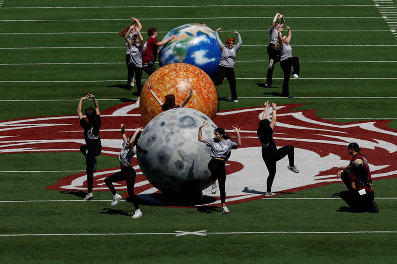 Люди танцуют рядом с изображениями Земли, Солнца и Луны на стадионе в Карбондейле (США)