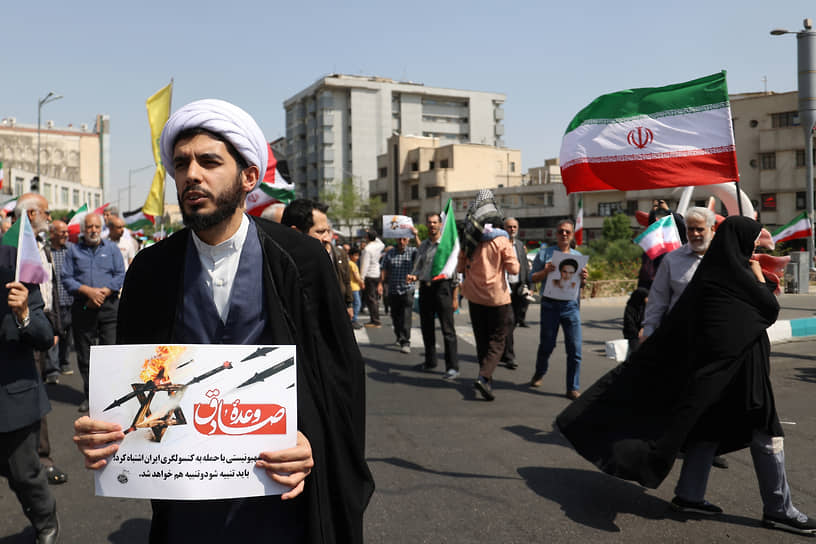 Иранский священнослужитель держит антиизраильский плакат во время митинга в Тегеране