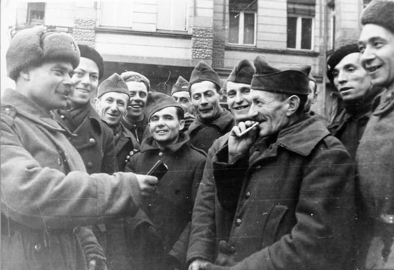 Советский солдат угощает папиросами освобожденных французских военнопленных 8 мая 1945 года