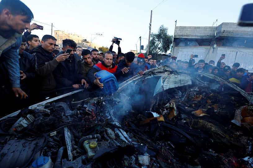Палестинцы возле автомобиля, уничтоженного в результате израильского обстрела Рафаха