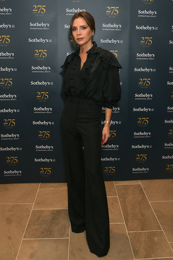 Виктория Бэкхем не изменяет своему стилю – на коктейле аукционного дома Sotheby&#39;s дизайнер была в своих любимых брюках клеш и черной блузке с пышными рукавами. 