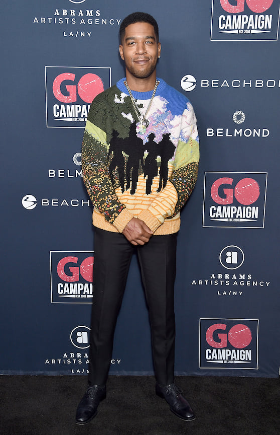 Музыкант Kid Cudi демонстрирует сдержанный и современный вариант “рэперского” аутфита  - золотая цепь, яркий свитер свитер в сочетании с брюками и туфлями. 