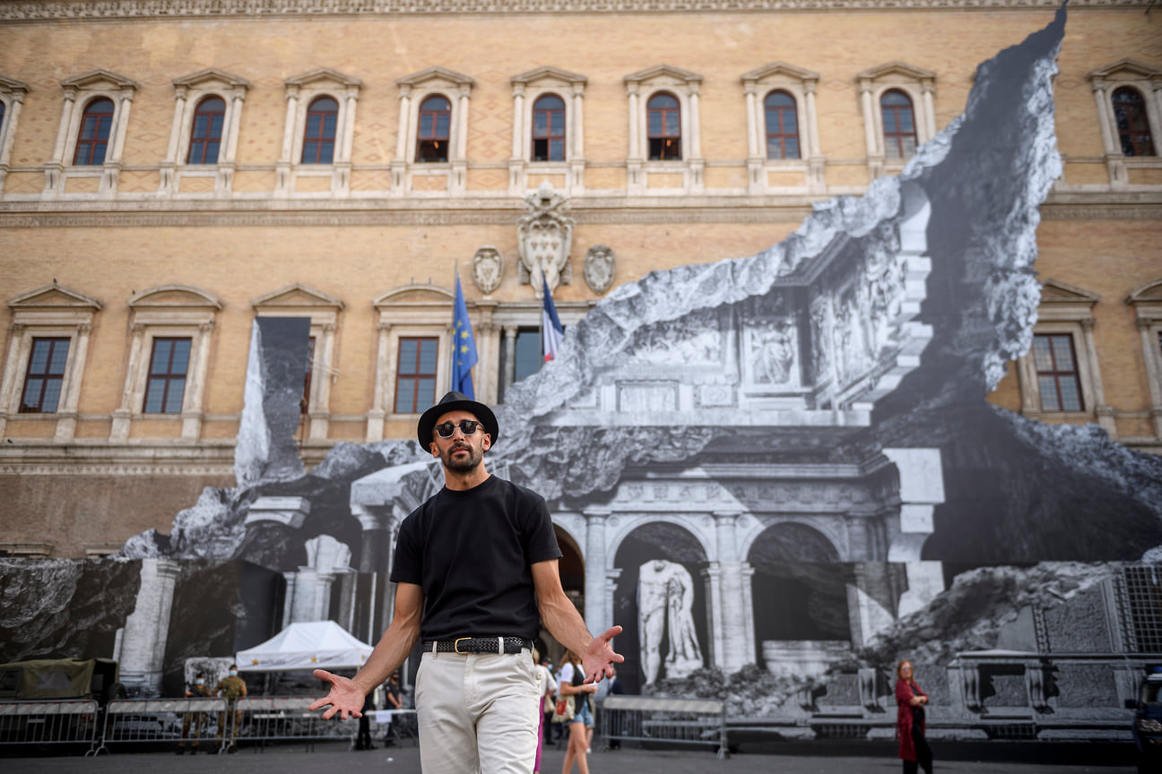 JR позирует перед своей художественной инсталляцией «Punto di Fuga» (Точка побега) на фасаде Палаццо Фарнезе Риме, 2021 год.
