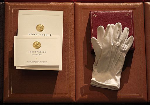 Нобелевскому лауреату вручается диплом (на фото слева), медаль (на снимке справа, в коробочке, под перчатками) и чек на 10 млн шведских крон (не представлен на фотографии)