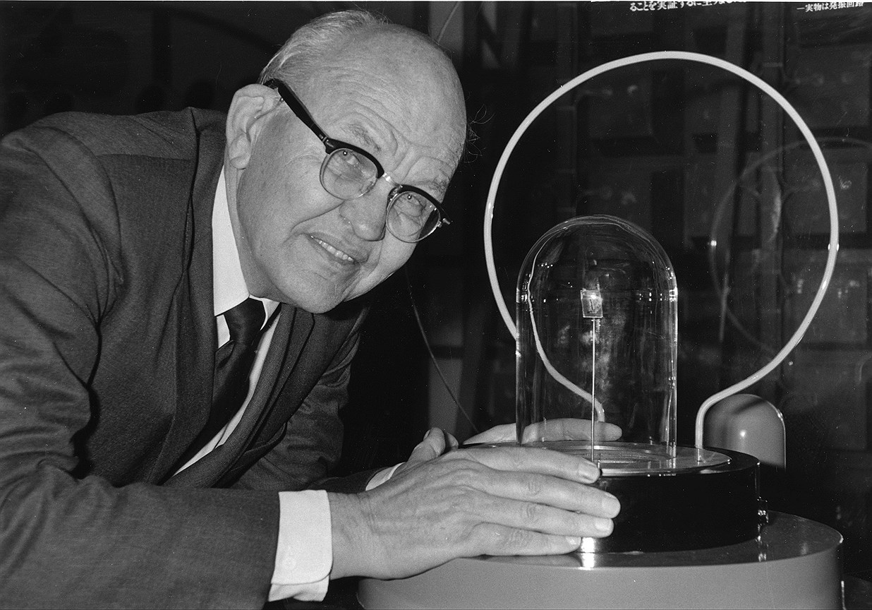 Джек Килби с оригиналом своего изобретения — помещенной в стеклянный колпак первой интегральной схемой, 1985 год