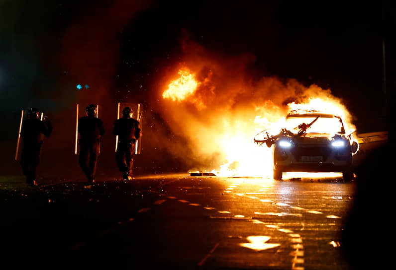 Полицейские проходят мимо горящей машины 