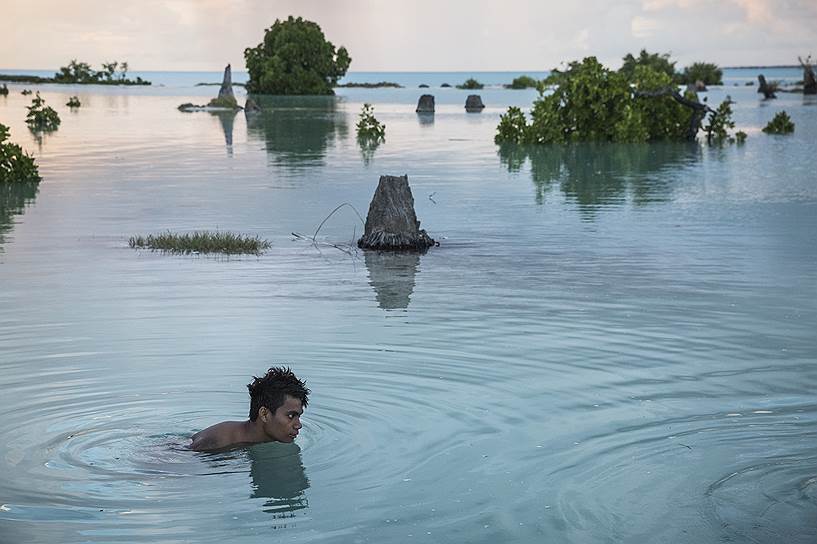 Юноша плывет по затопленной деревне на одном из островов Кирибати. Это государство в Тихом океане более других страдает от климатических изменений 