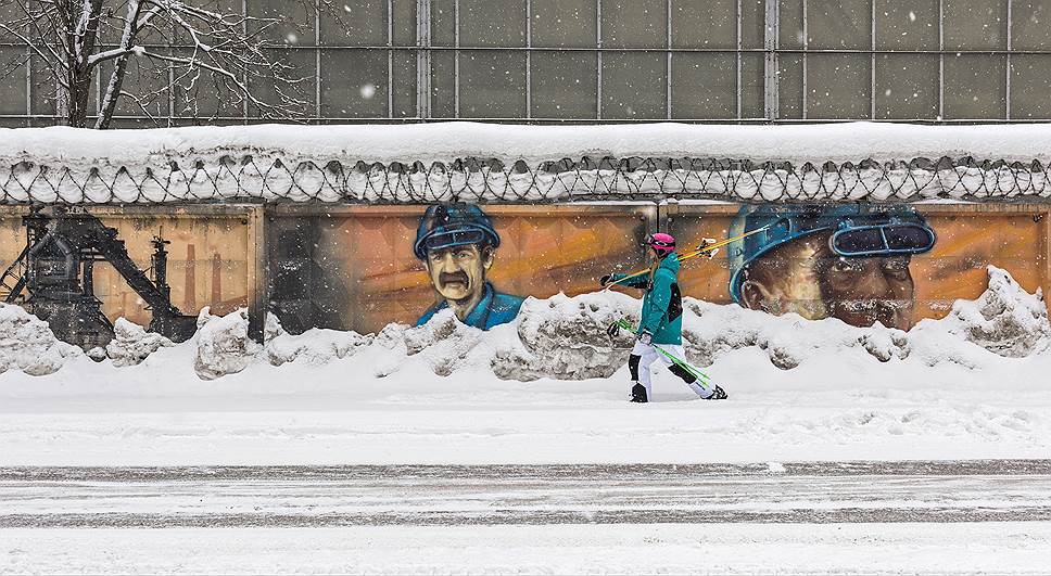 Кристина Лобастова у Чусовского металлургического завода, стена которого покрыта граффити с изображениями металлургов и героев советского времени  
