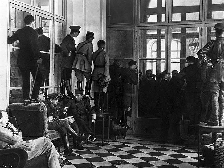 Офицеры союзников стоят на стульях и столах, чтобы заглянуть в Зеркальный зал, где подписывается Версальский мирный договор
