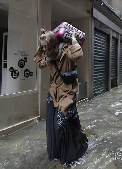 Туристка несет свой чемодан по затопленной улице 