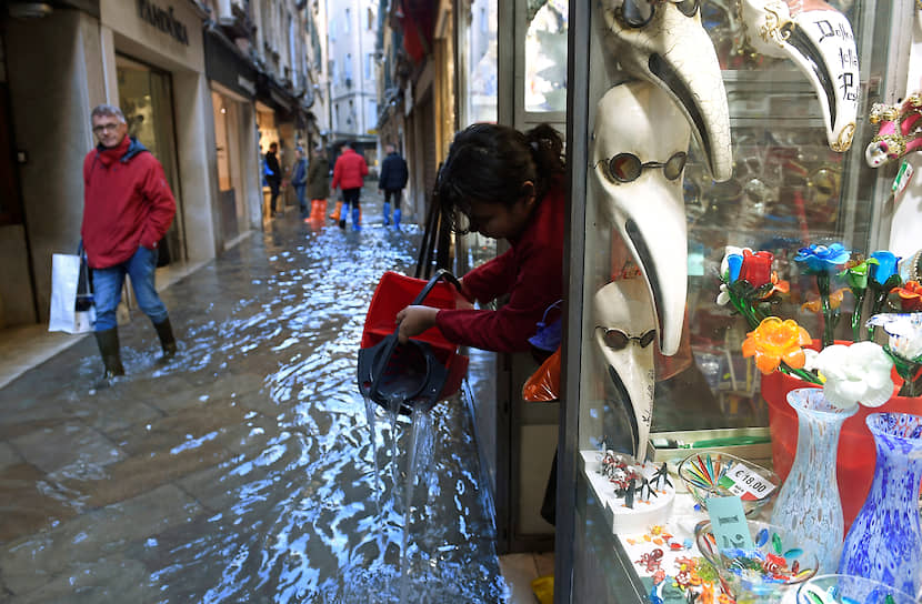 Женщины выливает воду из магазина на затопленный тротуар