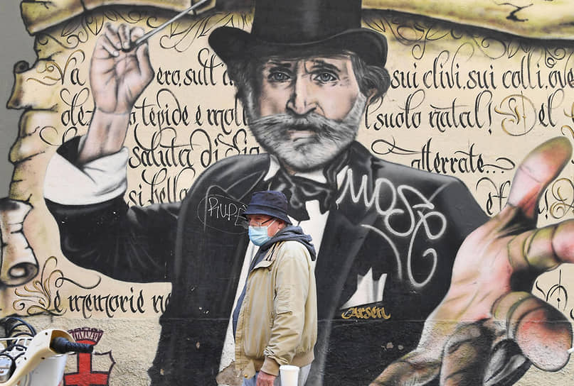 Ковид оглушает. Прохожий в защитной маске на фоне граффити — портрета композитора Джузеппе Верди в Милане